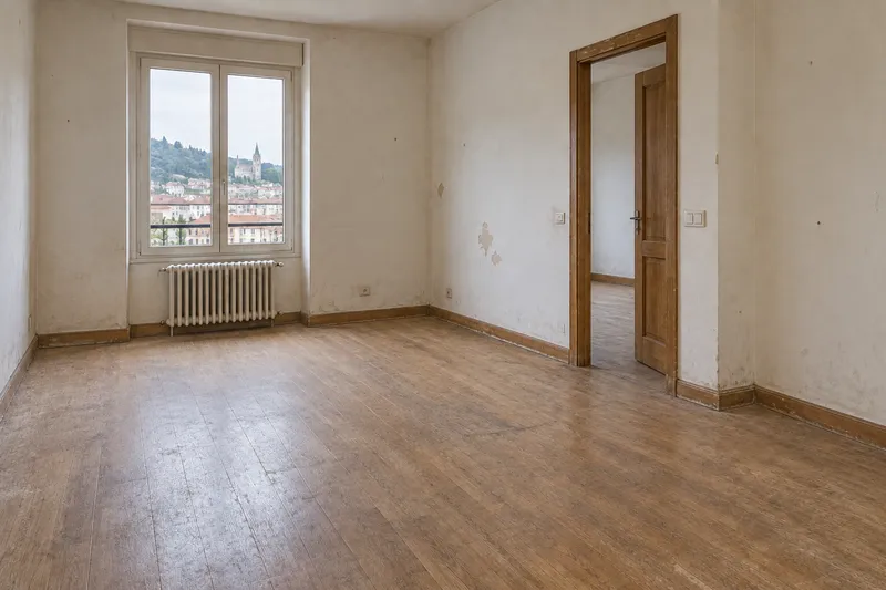 Salón de vivienda antigua con parquet desgastado, radiador y paredes pendientes de renovar